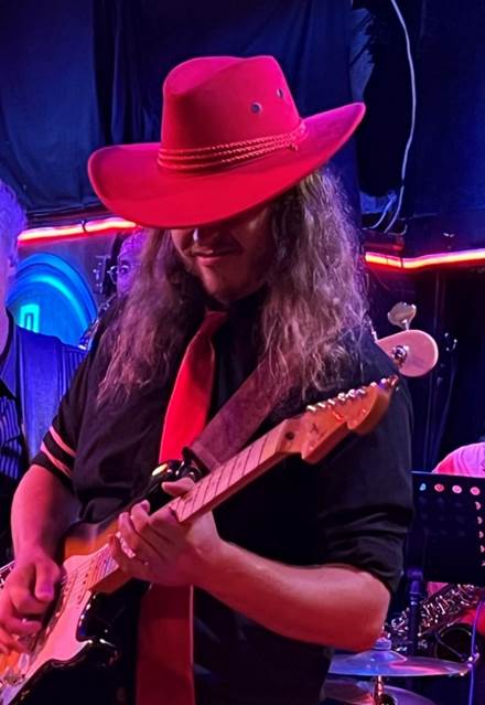 A person in a red hat playing a guitar

Description automatically generated